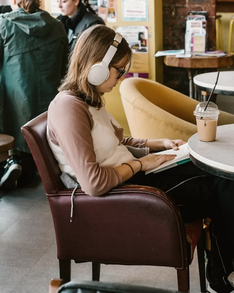 A young woman in headphones works through her notes in a busy café.