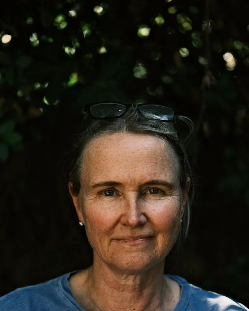 A woman in her fifties with glasses pushed up on her head, smiling softly in the evening light.
