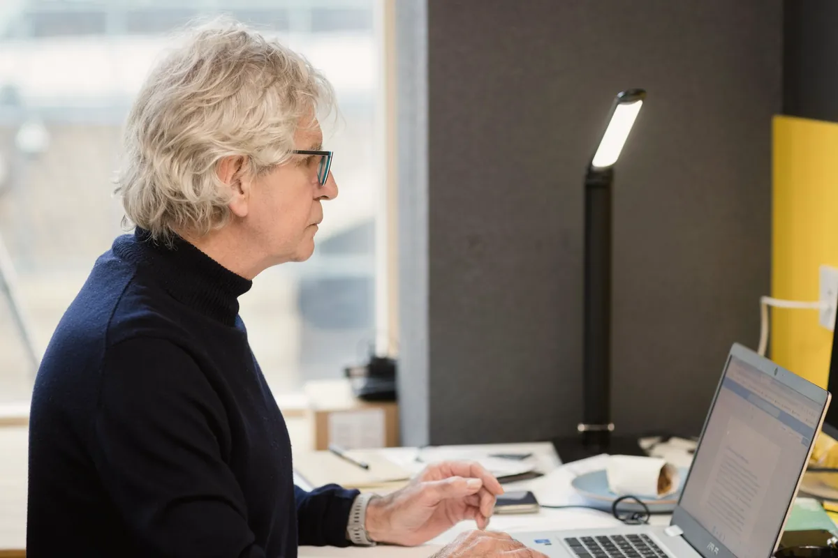 A woman with short grey hair works at her laptop at a desk, reading the screen.